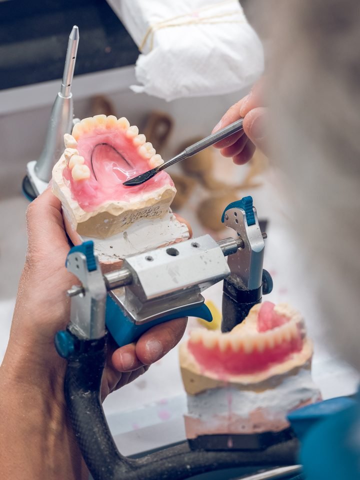 Protésico ajustando una prótesis completa sobre el articulador, en el laboratorio